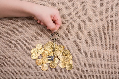 Hand holding a retro styled key over fake gold coins