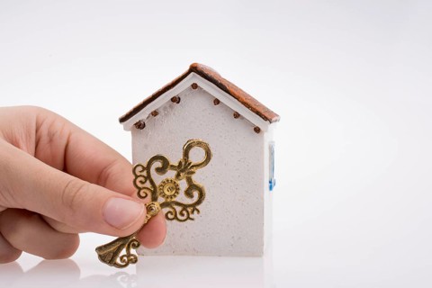 Hand holding a golden key near a house on a white background