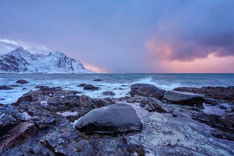 Beach of Norwegian sea on rocky coast in fjord on sunset in winter. Vareid beach