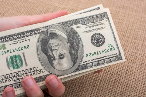 Hand holding banknote bundle of US dollar on a linen canvas background