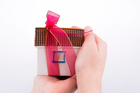 Hand holding a model house with a pink ribbon