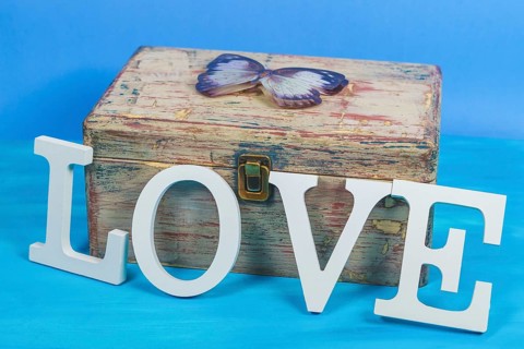 Word love written in white wooden letters on an antique wooden chest with a butterfly on top and a blue background