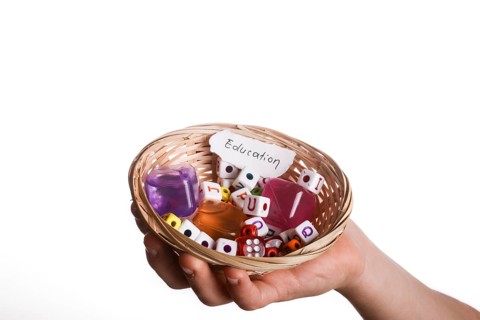 Child hand holding a education written a piece of torn paper in a basket full of letter cubes
