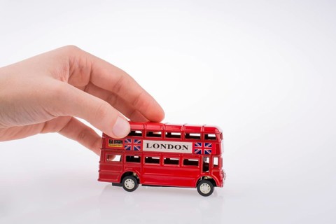 Child hand playing with London double decker bus model on white background