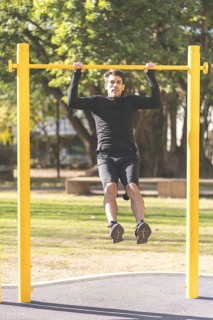 Young man doing pull ups on a crossbar at a park