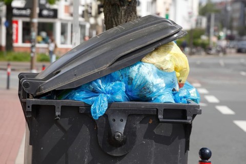 Filled rubbish container with open flap standing by the road