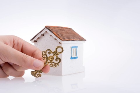Hand holding a golden key near a house on a white background