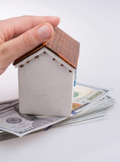 Hand holding a model house by the side of Turkish Lira banknotes on white background