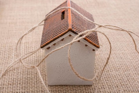 Thread wrapped around a model house on a brown background