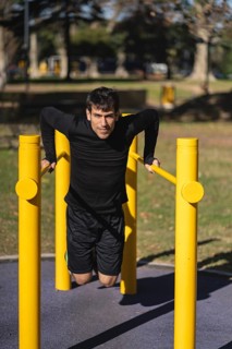 Fit young man doing push ups on horizontal bar outdoors