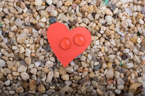Water drops on a heart shaped paper on sand background