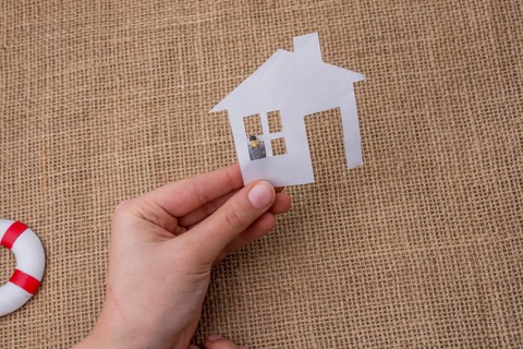 Paper house and a man figurine on a linen canvas background