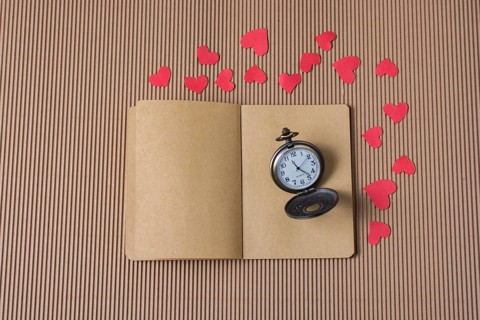 Retro Pocket watch on notebook with red paper hearts around