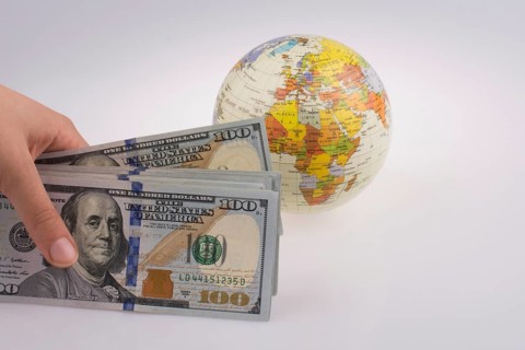 Human hand holding American dollar banknotes by the side of a model globe on white background