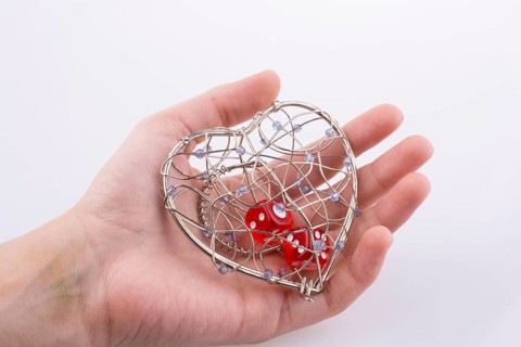 Hand holding Red dice in a heart shaped cage on a white background