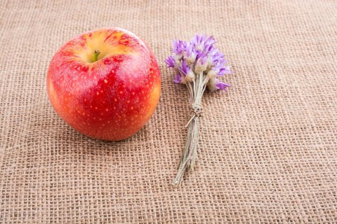 Tiny flower bouquet beside an apple on canvas