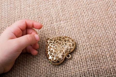 Heart shaped gold color metal object beside a hand