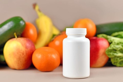 White food nutrition supplement bottle in front of fruits and vegetables in blurry background