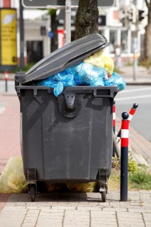 Filled rubbish container with open flap standing by the road