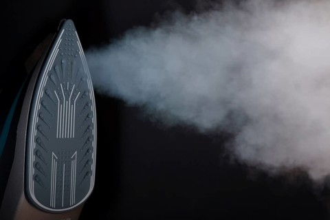 Iron seen from the front with steam coming out of its orifices on a black background