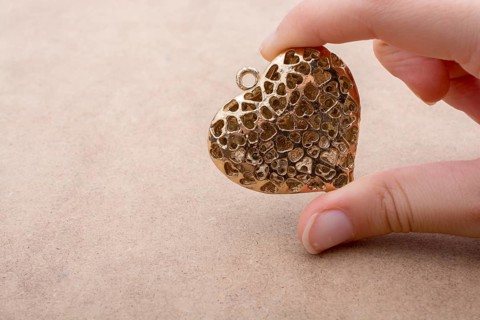 Heart shaped gold color metal object in hand