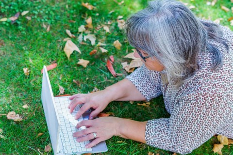 Top view of a white-haired woman working on her laptop computer lying on the grass in a park