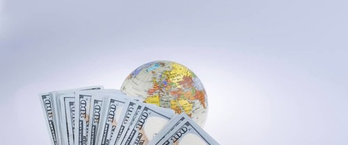 Human hand holding American dollar banknotes by the side of a model globe on white background