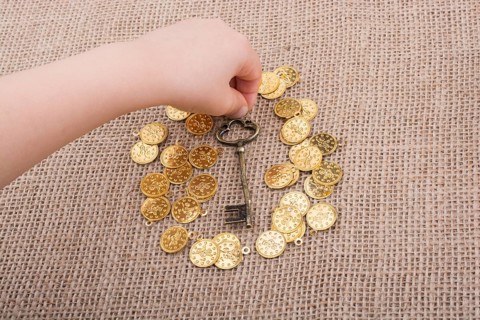 Hand holding a retro styled key over fake gold coins