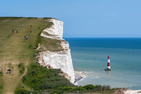 Tourists walking along the chalk cliffs overlooking Beachy Head lighthouse