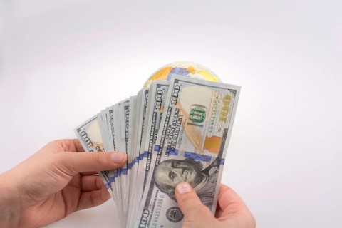Human hand holding American dollar banknotes by the side of a model globe on white background