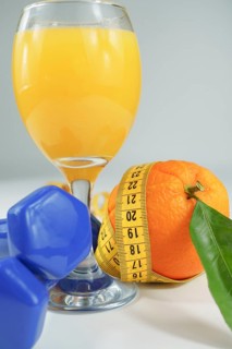 Orange with leaves surrounded by a tape measure with dumbbells and a glass of fresh orange juice