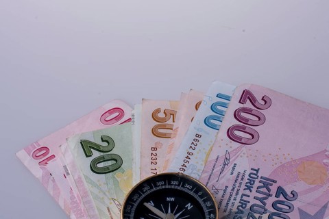 Turkish Lira banknotes by the side of a compass on white background