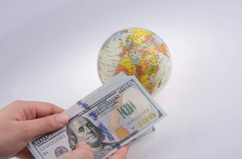 Human hand holding American dollar banknotes by the side of a model globe on white background
