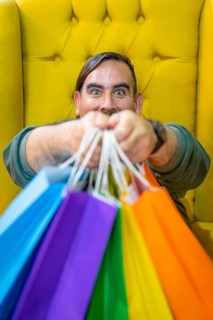 Happy man holding shopping bags on yellow background. Joy of consumption. Purchases