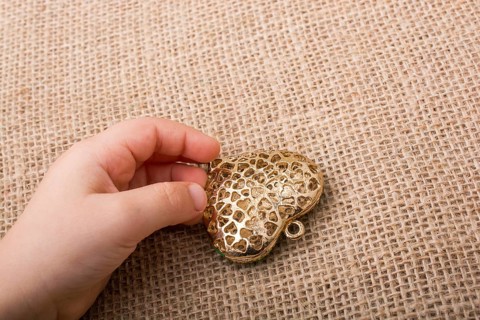 Heart shaped gold color metal object in hand