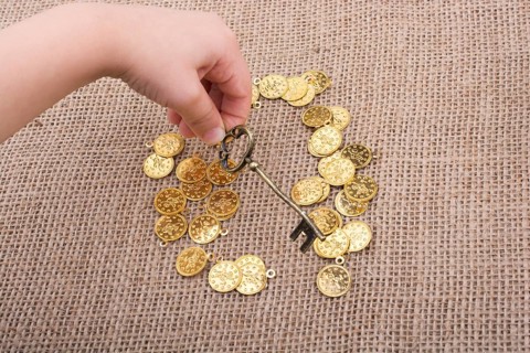 Hand holding a retro styled key over fake gold coins