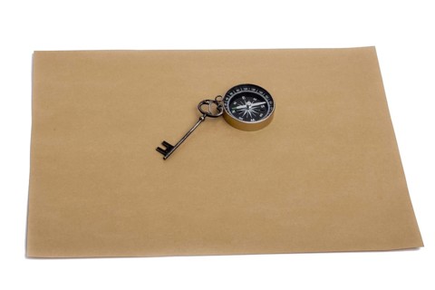 Key and compass on a sheet of colored plain paper with a white background