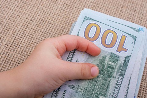 Toddler hand holding banknote bundle of US dollar on a linen canvas background