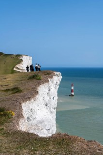 Tourists on the edge of the chalk cliffs overlooking Beachy Head lighthouse