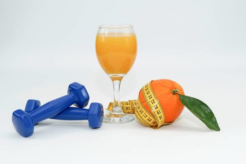 Orange with leaves surrounded by a tape measure with dumbbells and a glass of fresh orange juice