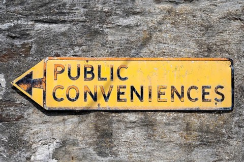 Signpost for public toilets in English on a house front