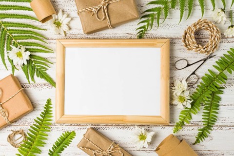 Elevated view blank frame surrounded by gifts leaves white flowers