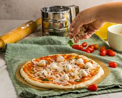Person sprinkling mozzarella cheese pizza
