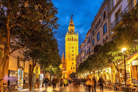 The lively pedestrian street Calle Mateos Gago and the Giralda bell tower of Santa Maria de la Sede Cathedral at dusk