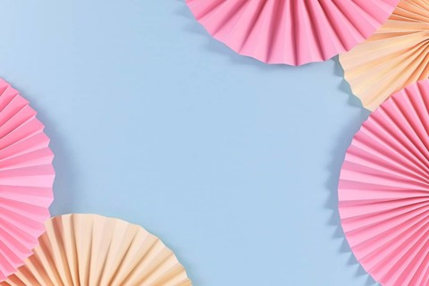 Beige and pink paper craft rosettes in corners of blue background with empty copy space in middle