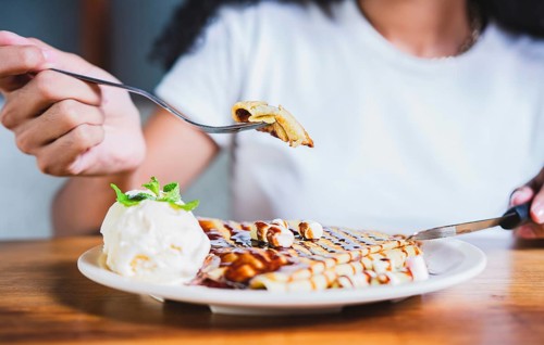 Close up of woman eating chocolate crepe and ice cream with fork. Hands of person with fork cutting chocolate crepe and ice cream