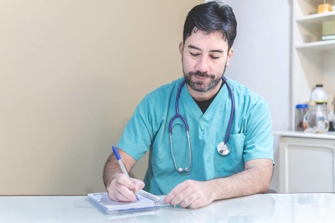 Latin doctor sitting at his desk taking notes