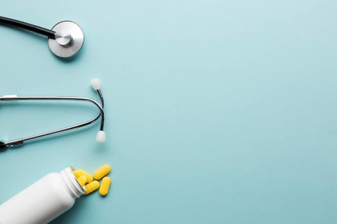 Yellow pills spilling out from white bottle near stethoscope blue surface