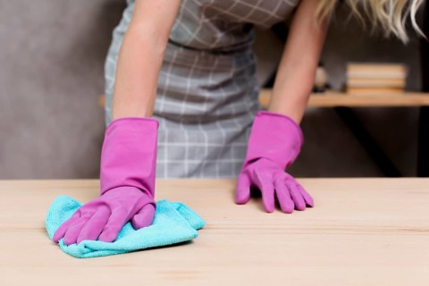 Midsection female janitor wiping wooden table with cloth