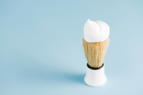 Overhead view classic shaving brush with white foam against blue background